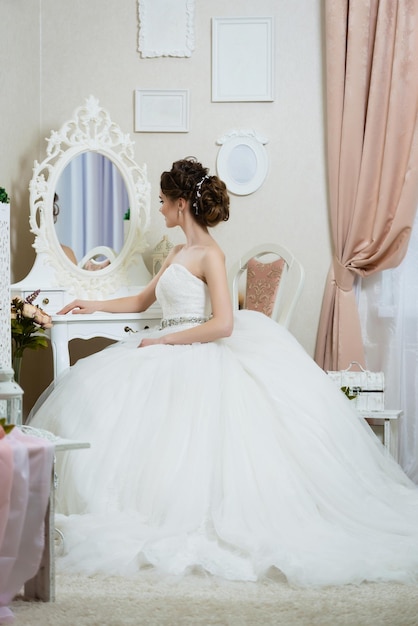 Hermosa joven novia frente al espejo Retrato con vestido de peinado de maquillaje de boda