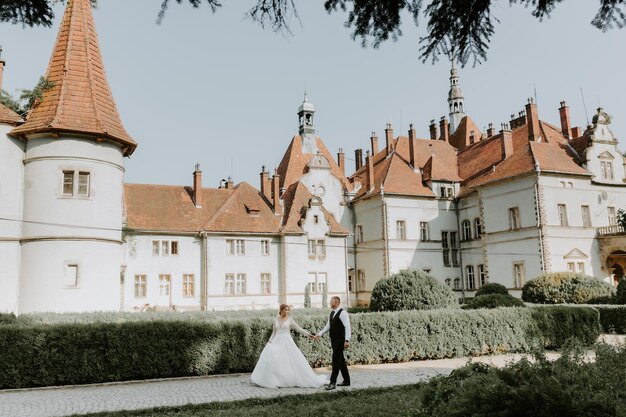 Hermosa joven novia mágica cogidos de la mano novio guapo bajo el arco del castillo