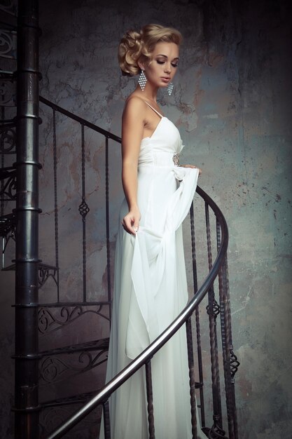Hermosa joven novia con un vestido blanco está de pie en una escalera de caracol Concepto de boda