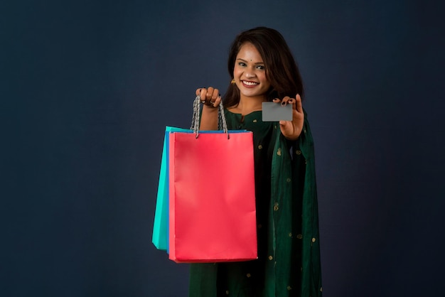 Hermosa joven o mujer sosteniendo y posando con bolsas de compras con tarjeta de crédito o débito en un fondo oscuro