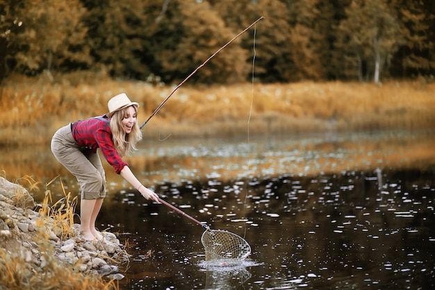 Hermosa joven en otoño por el río con una caña de pescar