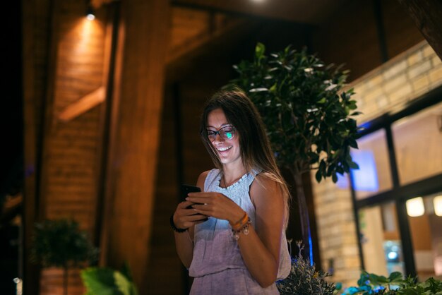 Hermosa joven parado afuera y mirando su teléfono celular. Sonriendo y mirando en el amor.