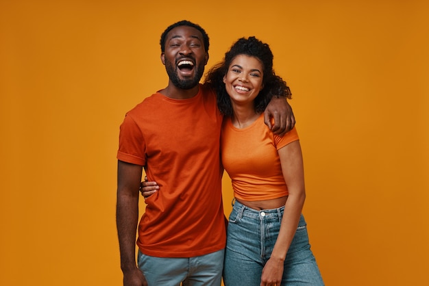 Hermosa joven pareja africana mirando a cámara y sonriendo mientras está de pie contra el fondo amarillo