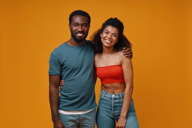 Hermosa joven pareja africana mirando a cámara y sonriendo mientras está de pie contra el fondo amarillo