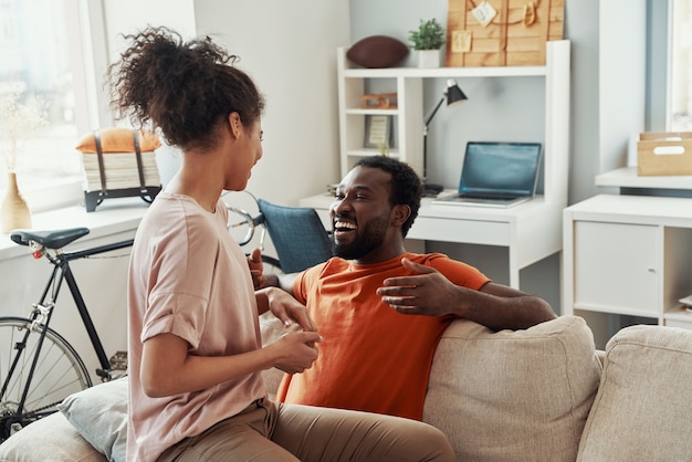 Hermosa joven pareja africana pegando y sonriendo mientras pasa tiempo en casa