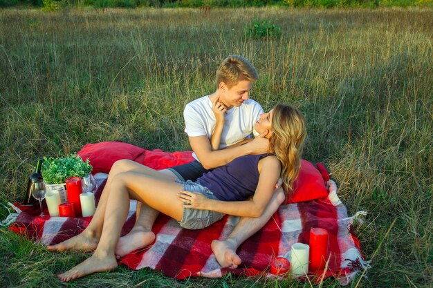 Hermosa joven pareja amorosa feliz en picnic acostado en cuadros en un día soleado de verano disfrutando y descansando. abrazándose y mirándose y sonriendo.