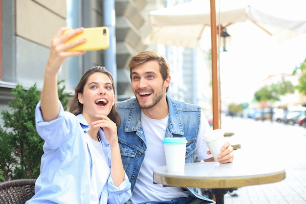 Hermosa joven pareja amorosa pegado entre sí en café mientras mujer haciendo selfie por teléfono inteligente.