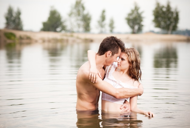 Hermosa joven pareja amorosa de pie en aguas tranquilas y mirando el uno al otro