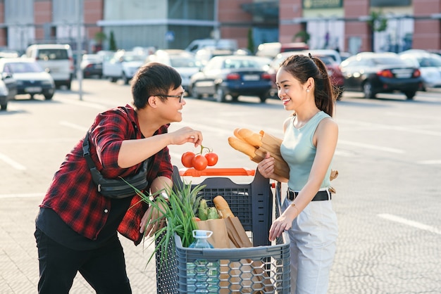 Hermosa joven pareja asiática comprobando los alimentos comprados en el carrito de compras cerca de la gran tienda