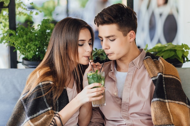 Hermosa joven pareja en un café! El niño y la niña beben un cóctel en la terraza de verano.