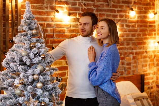 Hermosa joven pareja en casa decorando un árbol de Navidad.