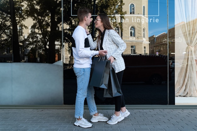 Hermosa joven pareja va de compras y lleva bolsas. El hombre y la mujer sostienen bolsas negras después de ir de compras.