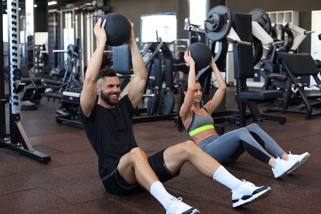 Hermosa joven pareja de deportes está trabajando con balón medicinal en el gimnasio.