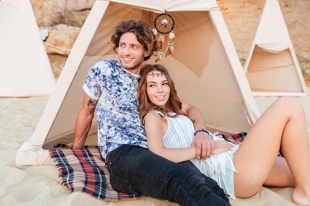 Hermosa joven pareja descansando juntos en tipi en la playa