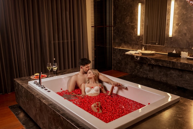 Hermosa joven pareja disfrutando de un baño con pétalos de rosa