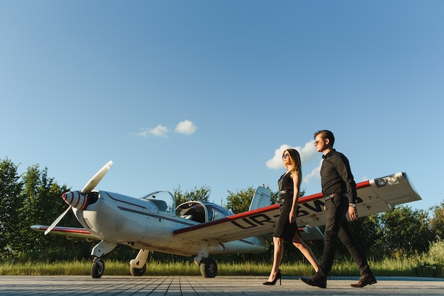 Hermosa joven pareja elegante en ropa oficial de pie cerca de avión privado