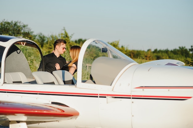 Hermosa joven pareja elegante en ropa oficial de pie cerca de avión privado