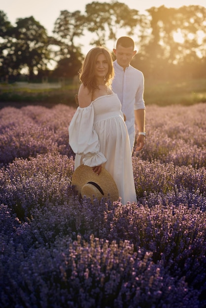 Hermosa joven pareja embarazada caminando en un campo de lavanda al atardecer Concepto de familia feliz