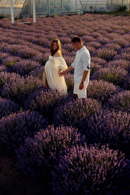 Hermosa joven pareja embarazada caminando en un campo de lavanda al atardecer Concepto de familia feliz