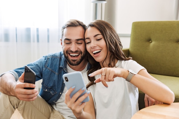 Hermosa joven pareja enamorada en casa, sentada en la sala de estar, apuntando al teléfono móvil