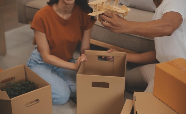 Hermosa joven pareja enamorada divirtiéndose desempaquetando cosas de cajas de cartón mientras se mudan juntos a su nuevo apartamento