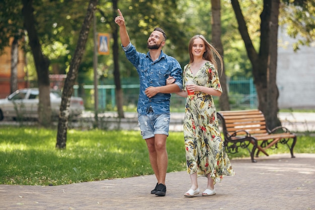 Hermosa joven pareja de enamorados caminando en el parque de verano con limonada fría. Pareja romántica en una cita al aire libre