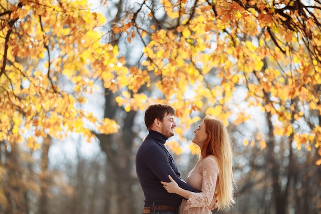 Hermosa joven pareja de enamorados sonriendo felizmente en el fondo de hojas amarillas en los árboles