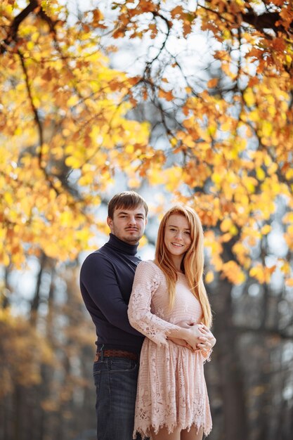 Hermosa joven pareja de enamorados sonriendo felizmente en el fondo de hojas amarillas en los árboles