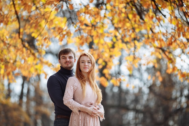 Hermosa joven pareja de enamorados sonriendo felizmente en el fondo de hojas amarillas en los árboles