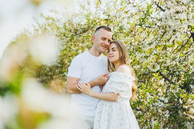 Una hermosa joven pareja esperando un embarazo en un lugar romántico, un huerto de manzanos en flor de primavera Feliz pareja alegre disfrutando mientras caminan en el jardín Un hombre sostiene la mano de una mujer