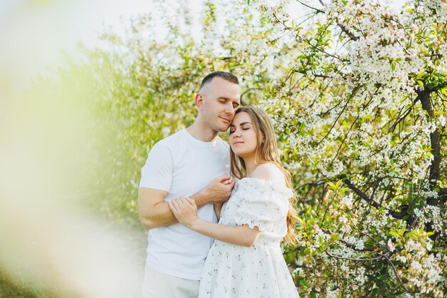 Una hermosa joven pareja esperando un embarazo en un lugar romántico, un huerto de manzanos en flor de primavera Feliz pareja alegre disfrutando mientras caminan en el jardín Un hombre sostiene la mano de una mujer