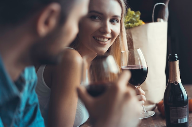 Hermosa joven pareja está bebiendo vino y sonriendo mientras cocina en la cocina de su casa.