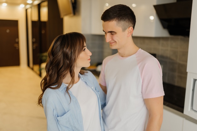 Hermosa joven pareja está mirando el uno al otro y sonriendo mientras pasan tiempo juntos en la cocina en casa. Concepto de pareja amorosa.