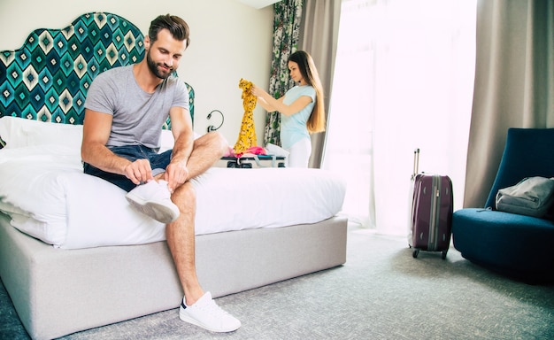 Hermosa joven pareja feliz en una habitación de hotel de lujo de buen humor están desempacando cosas