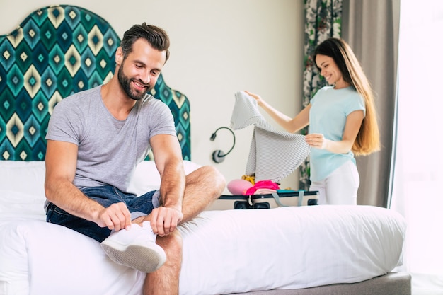 Hermosa joven pareja feliz en una habitación de hotel de lujo de buen humor están desempacando cosas