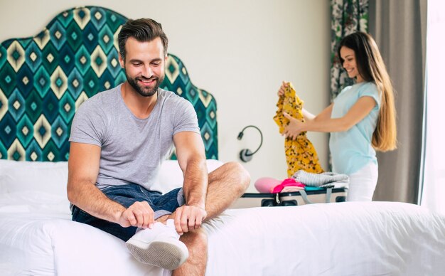 Hermosa joven pareja feliz en una habitación de hotel de lujo de buen humor están desempacando cosas