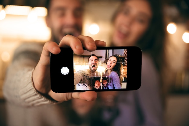 Hermosa joven pareja feliz pasar una velada romántica juntos en casa, bebiendo vino tinto, tomando un selfie