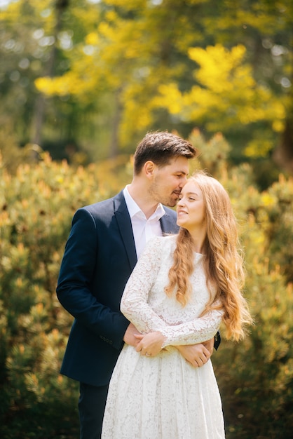 Hermosa joven pareja feliz y recién casada abrazando al aire libre en un día soleado