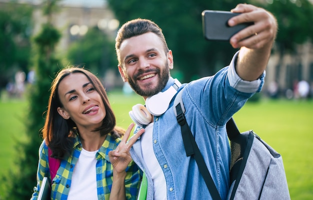 Hermosa joven pareja feliz en ropa casual con mochilas está haciendo foto selfie en smartphone