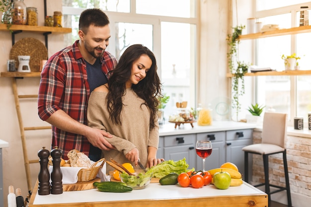 Hermosa joven pareja feliz sonriente está hablando y sonriendo mientras cocina alimentos saludables en la cocina en casa.