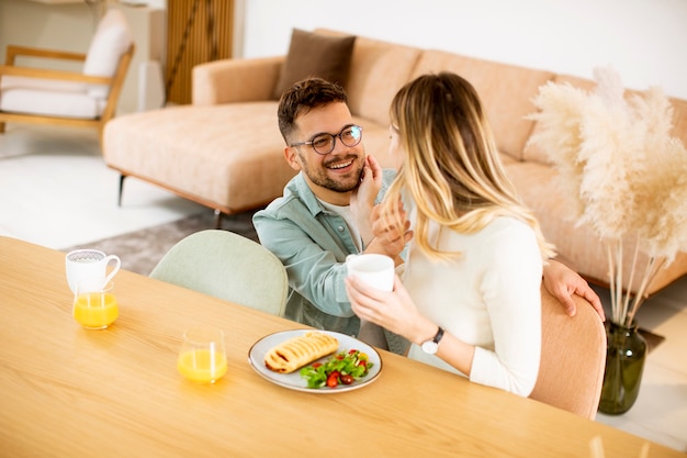 Hermosa joven pareja hablando y sonriendo mientras come saludable en casa.