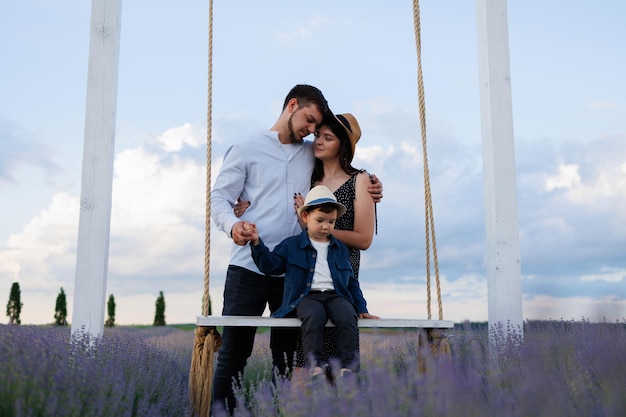 Hermosa joven pareja con hijo en un columpio en un campo de lavanda