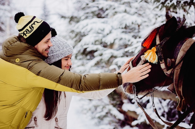 Hermosa joven pareja en invierno acaricia un caballo
