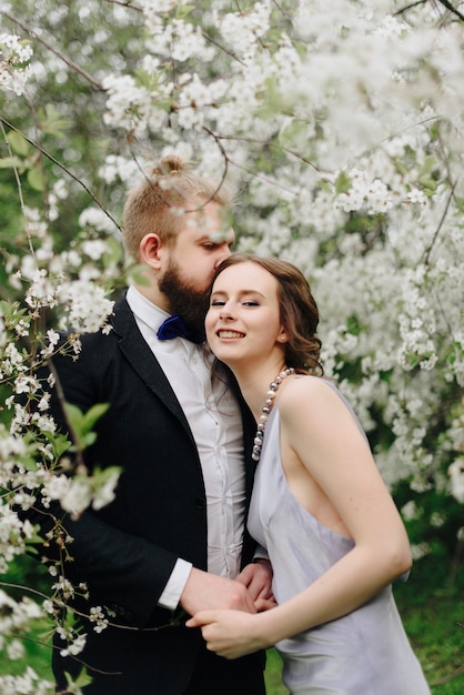 Hermosa joven pareja en el jardín con el telón de fondo de los cerezos en flor 1