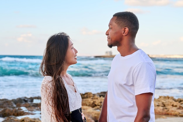 Hermosa joven pareja mirando a los ojos de perfil en el paisaje marino