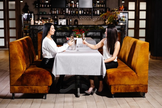 Hermosa joven pareja de mujeres con copas de champán están celebrando en un restaurante de lujo