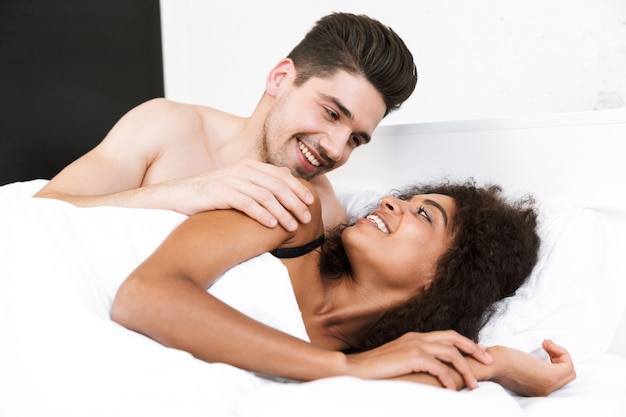 Hermosa joven pareja multiétnica feliz descansando en la cama debajo de la manta