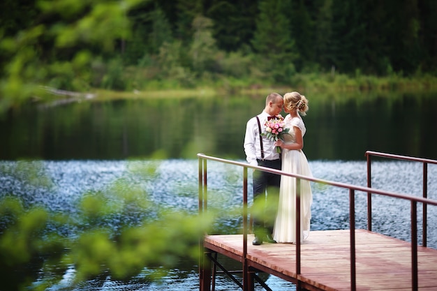 Hermosa joven pareja, novia y el novio posando en el fondo del lago. El novio y la novia en el muelle.