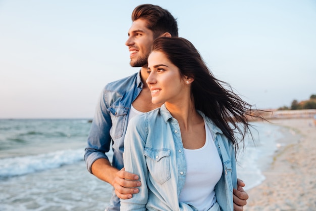 Hermosa joven pareja de pie y mirando las olas en la playa