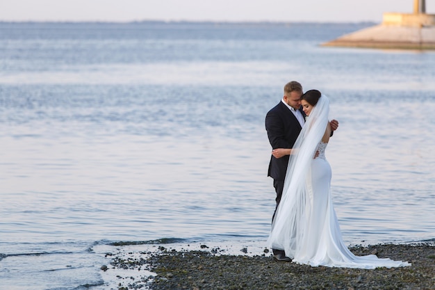 Hermosa joven pareja de pie en la orilla del mar